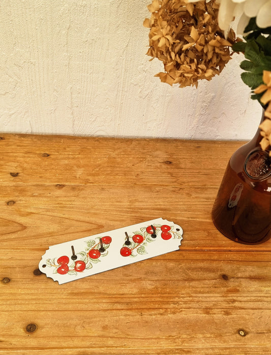 Porte torchons mural vintage en tôle émaillée blanche avec décor de cerises rouges et quatre crochets noirs