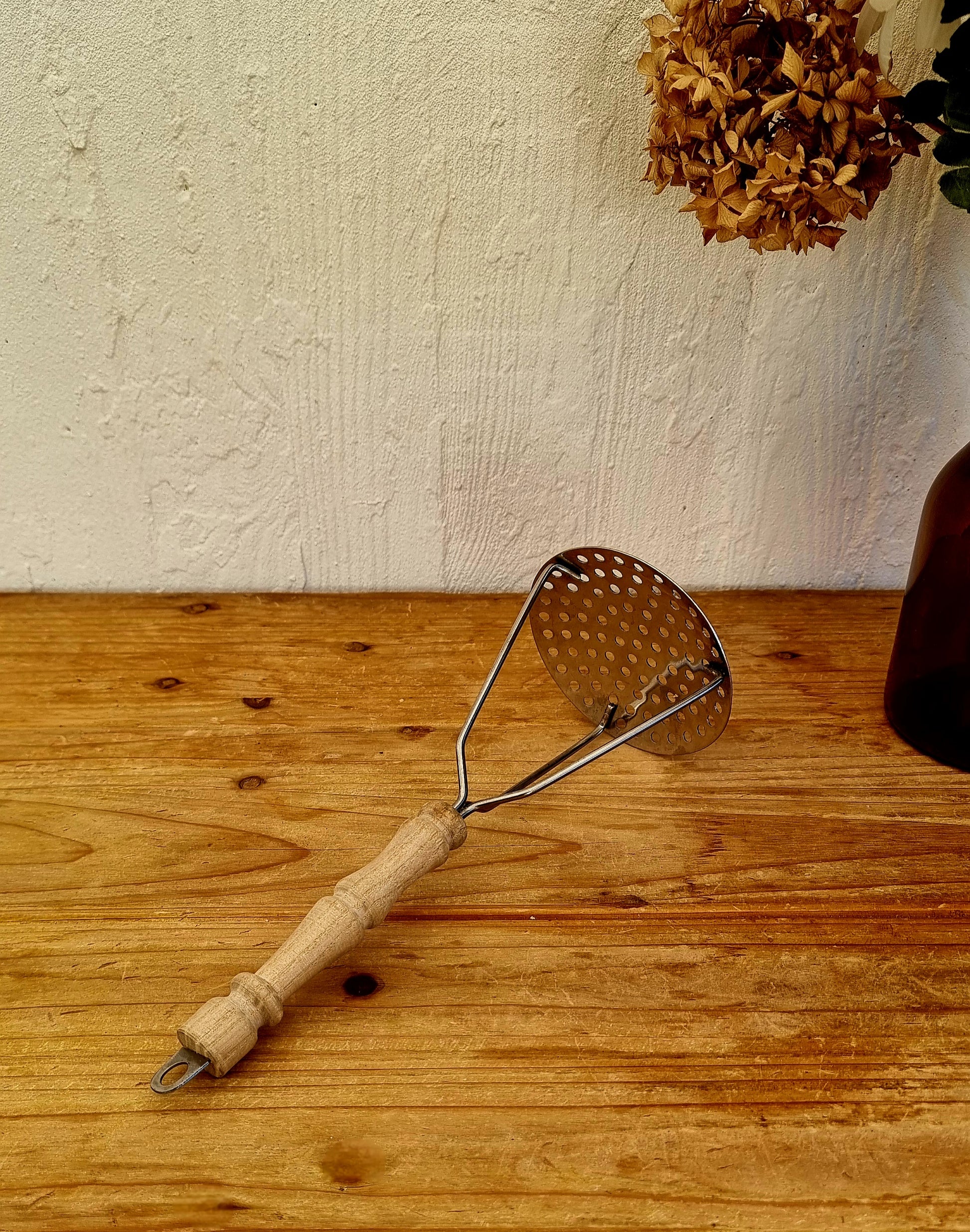 Presse-purée rétro avec manche en bois vintage posé sur une table en bois ambiance cuisine ancienne rétro